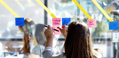 Lady placing Post-it® Super Sticky Note, 3 in. x 3 in. on glass wall to share tasks record capture with team others or projects