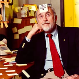 Pesquisador sentado em sua mesa de trabalho rodeado de papéis e anotações durante os anos 1980