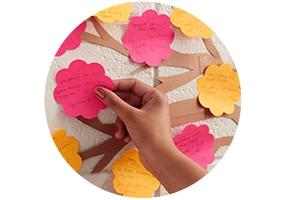 Mão colocando notas adesivas Post-it em formato de flor sobre uma parede
